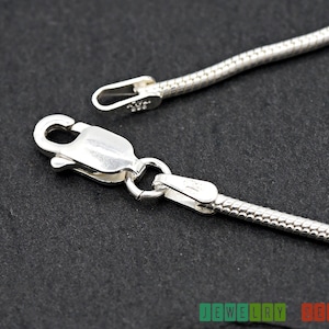 K&ouml;nnte beinhalten: Eine silberne Schlangenkettenhalskette mit einem Karabinerverschluss. Die Kette ist etwa 1,5 mm breit.