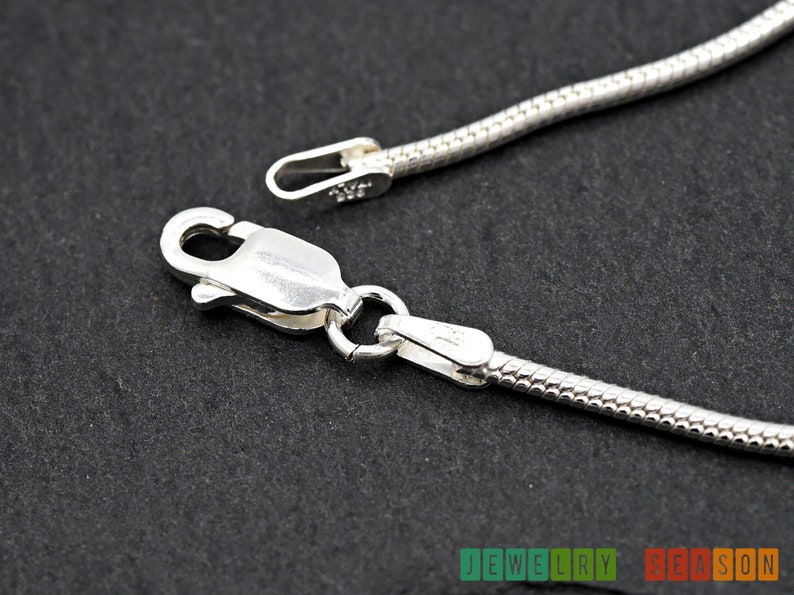 K&ouml;nnte beinhalten: Eine silberne Schlangenkettenhalskette mit einem Karabinerverschluss. Die Kette ist etwa 1,5 mm breit.
