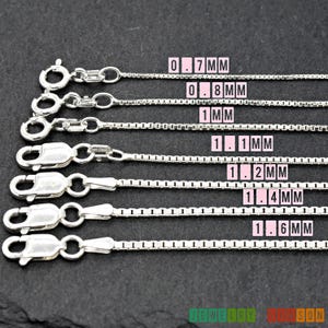May include: Six silver chains of varying thicknesses, laid out horizontally on a black surface. The chains are labelled with their thickness in millimetres: 0.7 mm, 0.8 mm, 1 mm, 1.1 mm, 1.2 mm, 1.4 mm, and 1.6 mm.