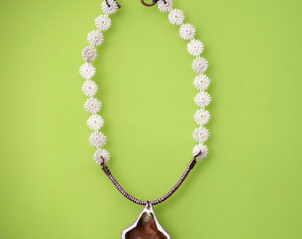 May include: A white crocheted necklace with a brown and white pendant. The pendant is shaped like a shell.