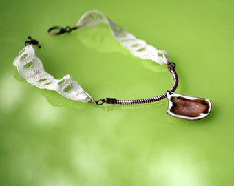 May include: A white lace necklace with a brown metal chain and a brown and white pendant. The pendant is shaped like a leaf and has a white center.