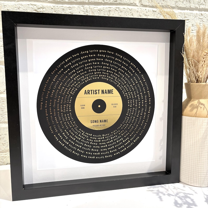 May include: A black framed print of a gold record with the text "ARTIST NAME" and "SONG NAME" in the center. The record is surrounded by a circle of gold text that says "Song Lyrics goes here" repeated many times.