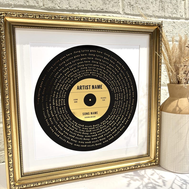 May include: A framed black and gold record with the song title "SONG NAME" and the artist name "ARTIST NAME" printed in gold lettering. The record is surrounded by a gold frame.