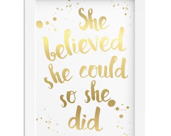 Puede incluir: Impresión enmarcada en blanco con letras doradas en relieve que dicen "She believed she could so she did". El fondo es blanco con salpicaduras doradas.
