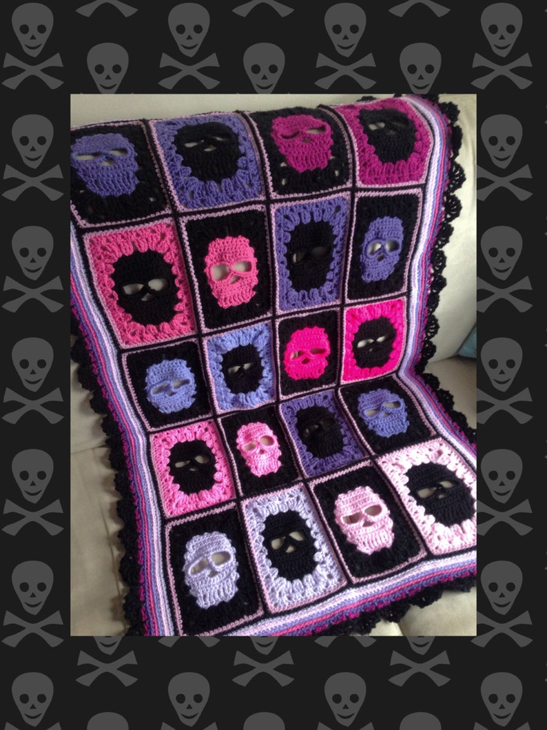 May include: Crocheted blanket featuring a repeating skull pattern in black, pink, purple, and white. The blanket has a black border with a scalloped edge. The skulls are centered in black squares, creating a unique and eye-catching design.