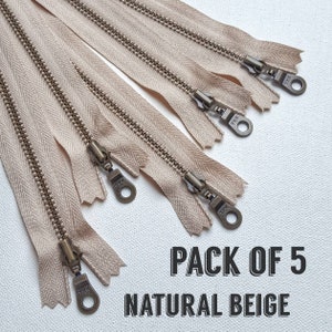 Könnte beinhalten: Packung mit 5 Reißverschlüssen in Naturbeige mit antiken Messing-Zierbändern.