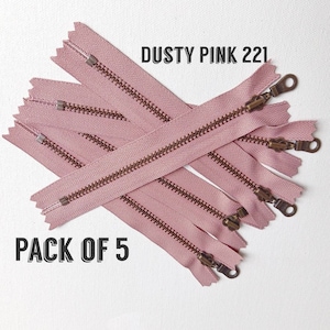 May include: A pack of five dusty pink zippers with brass sliders. The zippers are arranged in a criss-cross pattern and the text "DUSTY PINK 221" and "PACK OF 5" is visible.