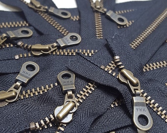 Könnte beinhalten: Nahaufnahme eines Stapels schwarzer Reißverschlüsse mit Messing-YKK-Schiebern. Die Reißverschlüsse sind in einem zufälligen Muster angeordnet, wobei einige der Schieber nach oben und einige nach unten zeigen.