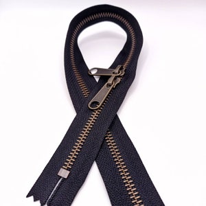 May include: A black zipper with brass teeth and a brass slider. The zipper is folded in half and the slider is in the middle of the zipper.