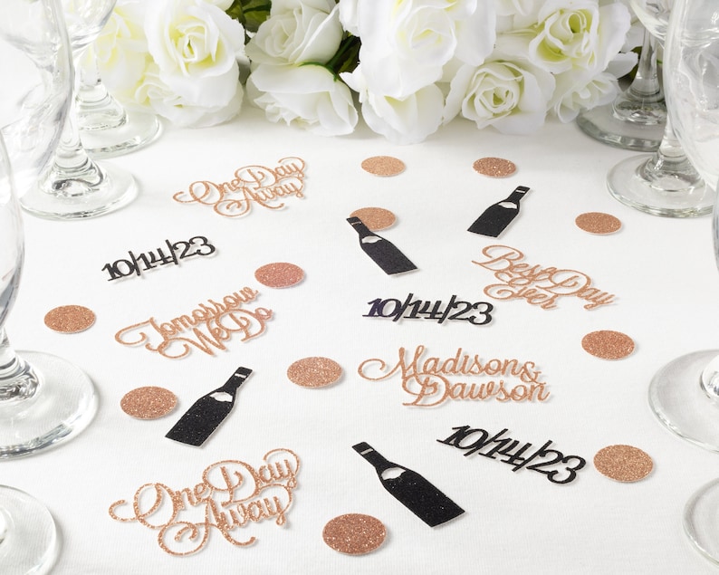 May include: Wedding table confetti with rose gold glitter and black lettering. The confetti includes the date 10/14/23, the words "One Day Away", "Tomorrow We Do", "Best Day Ever", and "Madison & Dawson".