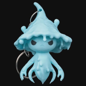 Puede incluir: Un llavero azul claro impreso en 3D con una criatura estilizada con cabeza de hongo y expresión severa. La figura tiene un anillo para sujetar y un diseño texturizado y goteante. El fondo es negro.