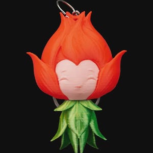 Könnte beinhalten: Ein skurriler, 3D-gedruckter Schlüsselanhänger mit einer stilisierten Blume mit lächelndem Gesicht. Die Blume hat leuchtend rote Blütenblätter, ein hellrosa Gesicht und grüne Blätter. Ein silberfarbener Ring ist angebracht.