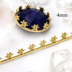 May include: A gold-colored metal setting with star-shaped accents surrounds a faceted, deep blue gemstone. A separate gold-colored metal strip with star-shaped embellishments is also visible. The text "4mm" is in the image, indicating the size of the gemstone.
