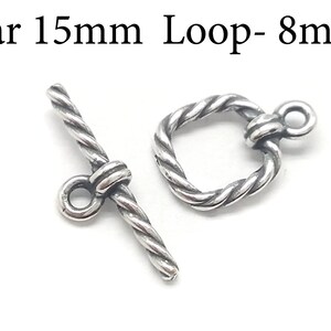 Könnte beinhalten: Silberfarbener Toggle-Verschluss mit einer 15 mm Stange und einer 8 mm Schlaufe. Die Stange und die Schlaufe sind beide im gedrehten Seil-Stil.