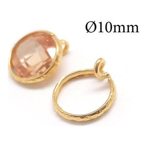 Puede incluir: Dos componentes de joyería en tono dorado con un diámetro de 10 mm. Una pieza presenta una piedra facetada de color melocotón claro en un marco dorado texturizado, mientras que la otra es un anillo circular dorado texturizado con una pequeña anilla.