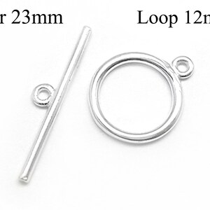 Könnte beinhalten: Silberner Toggle-Verschluss mit einer 23 mm langen Stange und einer 12 mm großen Schlaufe. Die Stange hat an einem Ende eine kleine Schlaufe. Die Schlaufe ist ein Kreis mit einer kleinen Schlaufe oben.