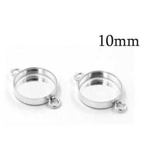 Puede incluir: Dos bases circulares de color plateado para joyería con dos pequeñas anillas en los lados opuestos para su fijación. Cada componente metálico redondo presenta un centro rebajado y lleva el texto 10mm, indicando el diámetro interior.