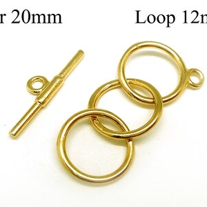 Könnte beinhalten: Goldfarbener Metall-Barverschluss mit einer 20 mm langen Stange und einer Schlaufe mit drei verbundenen Ringen, die jeweils einen Durchmesser von 12 mm haben. Die Schlaufe hat einen kleinen Ring an der Seite zum Anbringen an einer Kette oder Schnur.