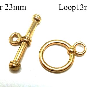 Könnte beinhalten: Goldfarbener Metallverschluss mit einem 23 mm langen Stab und einer 13 mm großen Schlaufe. Der Stab hat ein abgerundetes Ende und eine kleine Schlaufe an der Seite. Die Schlaufe ist ein einfacher Kreis mit einer kleinen Schlaufe an der Seite.