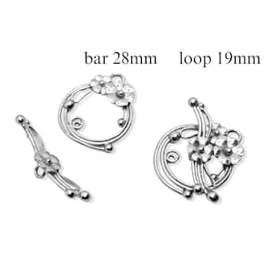Könnte beinhalten: Silberfarbene Metall-Schmuckverschlüsse mit floralen Designs. Die Verschlüsse umfassen eine 28 mm lange Stange und eine 19 mm große Schlaufe.
