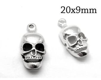 May include: Two silver-colored metal skull charms, each featuring a small loop at the top for attachment. The skulls have detailed eye sockets, nasal cavities, and teeth. The text 20x9mm is printed in black above the right skull charm.
