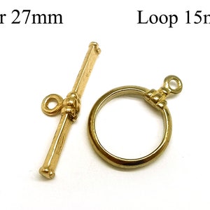 Könnte beinhalten: Goldfarbener Metallverschluss mit einer 27 mm Stange und einer 15 mm Schlaufe. Die Stange hat ein dekoratives Design und die Schlaufe ist rund.  Bar 27mm Loop 15mm