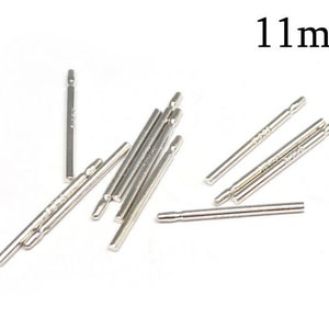 Può includere: Un gruppo di aste metalliche argentate, ciascuna lunga 11 mm. Le aste sono sparse su una superficie bianca.