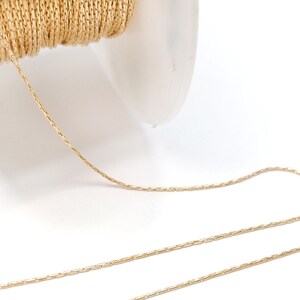May include: A spool of gold-colored chain, partially unwound, against a white background. The chain has a delicate, textured appearance, ideal for jewelry making or craft projects. The spool is white and translucent.