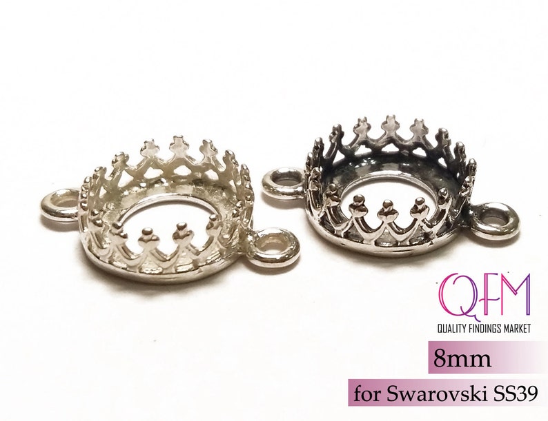 K&ouml;nnte beinhalten: Zwei kronenf&ouml;rmige Schmuckfassungen aus silberfarbenem Metall mit kreisf&ouml;rmigen &Ouml;sen an jeder Seite. Die Fassungen sind f&uuml;r 8mm Steine, speziell f&uuml;r Swarovski SS39, ausgelegt. Der Text QFM Quality Findings Market ist sichtbar.