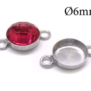 May include: A silver-toned metal bezel setting with two loops for attaching to jewelry. The bezel is designed to hold a 6 mm round cabochon stone. The setting is shown with a red cabochon stone.