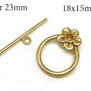 Könnte beinhalten: Goldfarbener Metall-Schiebeverschluss mit einer Stange von 23 mm und einem blütenförmigen Ring von 18 mm x 15 mm.