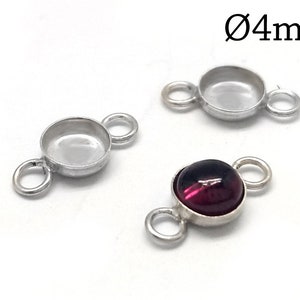 May include: Three silver-colored jewelry findings with a circular design. Two findings are empty, while the third features a 4mm diameter, deep red gemstone. Each finding has two small loops for attaching to other components.