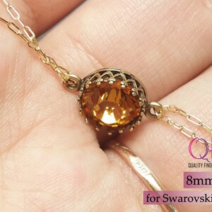 K&ouml;nnte beinhalten: Eine goldfarbene Metallfassung mit einem runden, facettierten bernsteinfarbenen Kristall. Die Fassung hat einen dekorativen gewellten Rand und ist an einer feinen Goldkette befestigt. Der Text auf dem Bild lautet 8mm for Swarovski SS39.