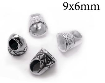 May include: Four silver-toned metal bead caps with a textured, intricate pattern on the exterior. Each piece is cylindrical with a flared opening and measures 9x6mm. The metal has a polished finish with dark recessed areas highlighting the design.