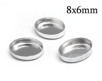 Puede incluir: Tres bases para cabujón ovaladas de color plateado con bordes elevados, cada una de 8x6mm. Estos pequeños componentes metálicos presentan una superficie interior lisa y reflectante, con un diseño sencillo de cuenco poco profundo para insertar piezas.