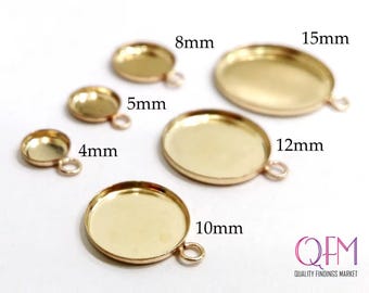 May include: A collection of six gold-toned metal jewelry pendant settings in various sizes, including 4mm, 5mm, 8mm, 10mm, 12mm, and 15mm. Each round or oval bezel cup features a small attached loop for hanging. The text QFM QUALITY FINDINGS MARKET is visible.
