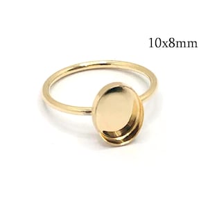 May include: A gold-toned metal ring blank featuring a smooth, oval-shaped bezel setting designed for a 10x8mm stone or cabochon. The ring has a thin, polished band and a raised, empty cup-like setting for jewellery making and customisation.