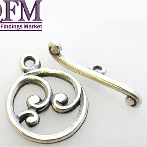 May include: Silver-toned metal clasp with a decorative swirl design. The clasp is made of two pieces, one with a circular design and the other with a curved shape.