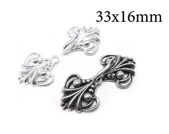 Könnte beinhalten: Drei silberfarbene Umhangverschlüsse aus Metall mit einem verzierten, fächerartigen Filigranmuster und kleinen kugelförmigen Akzenten. Die Teile messen 33x16mm. Zwei Einzelteile sind neben einem montierten Verschluss mit Haken zu sehen.
