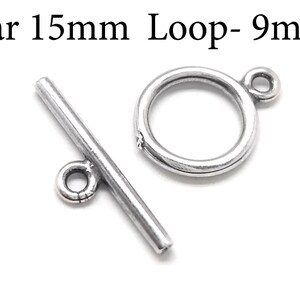 Könnte beinhalten: Silberner Toggle-Verschluss mit einem 15 mm langen Stab und einer 9 mm großen Schlaufe. Der Stab hat einen kleinen runden Ring am Ende. Die Schlaufe ist ein einfacher Kreis.