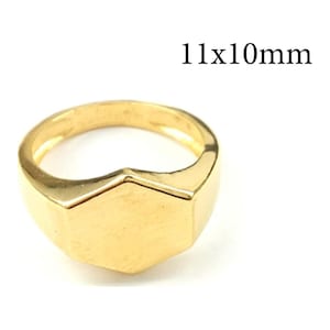 May include: A gold-toned signet ring featuring a smooth, flat hexagonal face. The ring has a polished metallic finish and a solid band. The text 11x10mm is printed in black above the ring, indicating the dimensions of the hexagonal face.