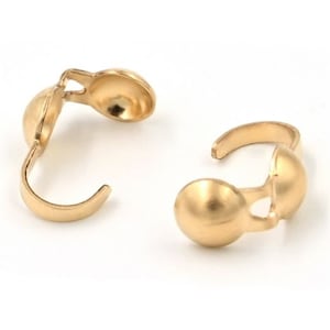 May include: Two gold-colored, open-ended jewelry clasps. Each clasp has a rounded ball shape connected to a curved hook. The clasps are designed to connect jewelry pieces.