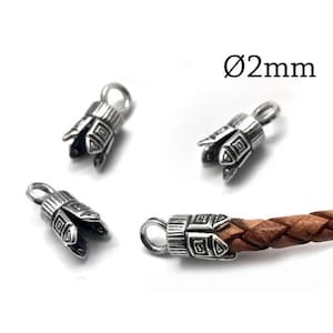 May include: Three silver-toned metal cord ends with a textured geometric pattern and a small loop at the top, alongside one cord end attached to a brown braided leather cord. The text Ø2mm is visible, indicating a 2mm diameter opening.