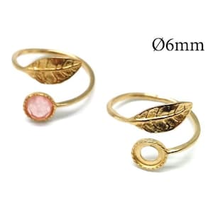 Può includere: Due anelli aperti color oro con un design a foglia su un'estremità e un castone circolare sull'altra. Un anello contiene una pietra rotonda rosa, mentre l'altro ha il castone vuoto. Il testo Ø6mm indica un diametro di 6 mm.