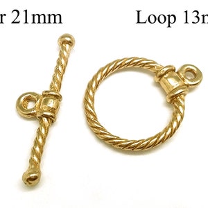 Pode incluir: Fecho de metal dourado com uma barra de 21 mm e um laço de 13 mm. A barra e o laço têm um design de corda torcida.