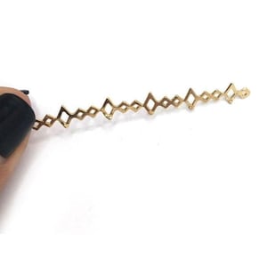 May include: A thin, gold-colored metal connector component featuring a repeating geometric pattern of interconnected diamond shapes. The delicate, elongated piece is designed with small loops at each end for attachment in jewelry making projects.