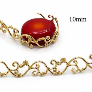 May include: Gold-colored filigree jewelry findings with a red cabochon stone. The findings include a decorative floral design and the text "10mm". The jewelry findings are suitable for crafting necklaces, bracelets, and earrings.
