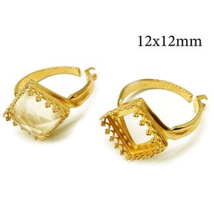 May include: Two gold-toned adjustable rings with square settings measuring 12x12mm. One ring features a faceted clear stone, while the other is an empty setting with a decorative scalloped edge. Both bands have a textured finish.