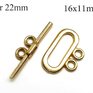 Könnte beinhalten: Goldfarbenes Schmuckverschluss-Set. Der Stab ist 22 mm lang, und der ovale Verschluss ist 16x11 mm groß. Das Set enthält einen Stab mit zwei Schlaufen und ein ovales Teil mit drei Schlaufen. Ideal für die Schmuckherstellung.