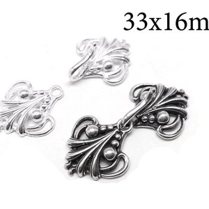 May include: Three silver metal decorative embellishments with a floral design. The embellishments are 33mm by 16mm.